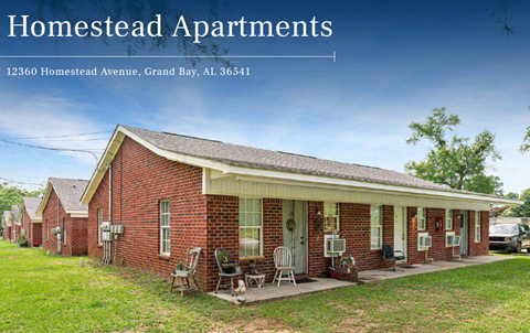 A red brick house with a porch and a sign that says "Homestead Apartments".