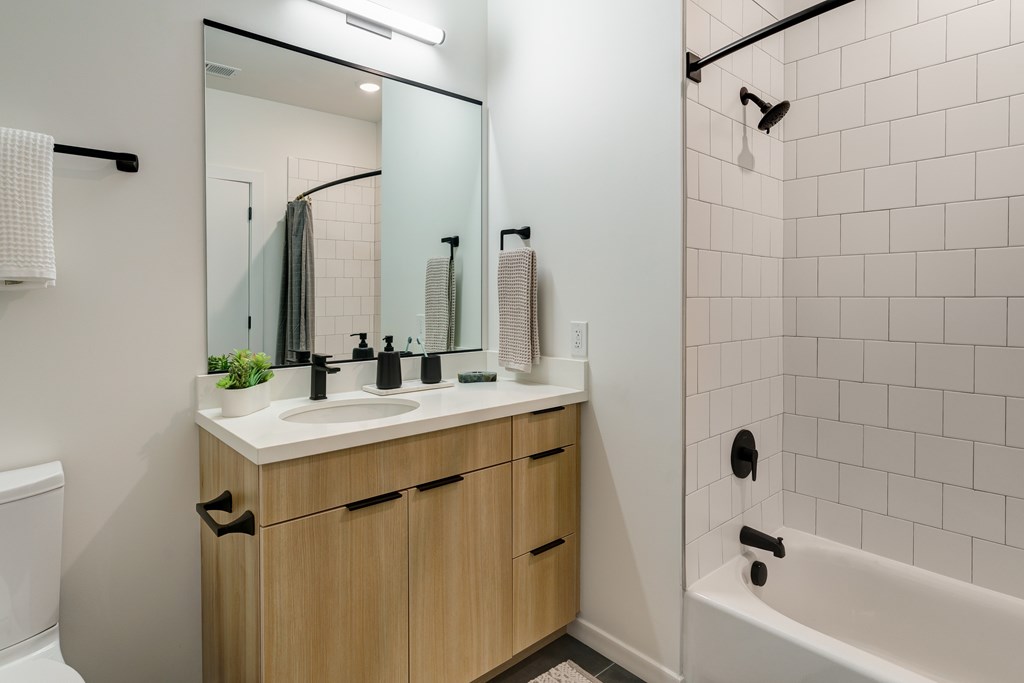 A bathroom with a white tub, sink, and a mirror.