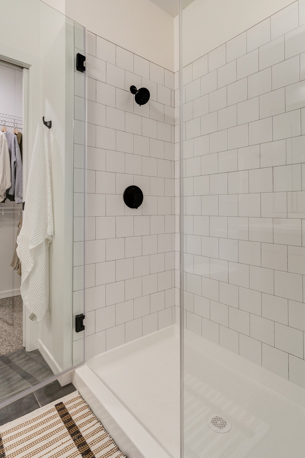 A white tiled shower with a white tub and a brown rug.