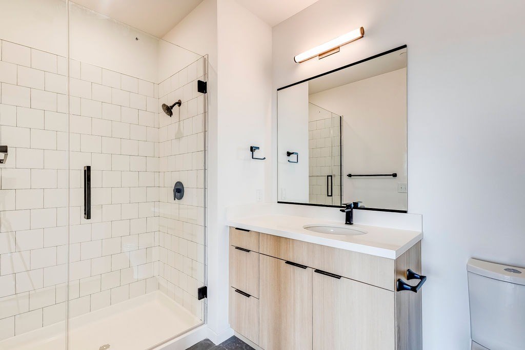A white tiled bathroom with a sink, mirror, and toilet.