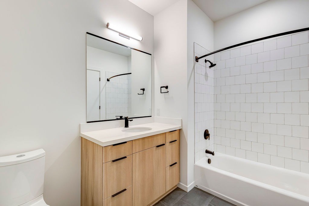 A white bathroom with a wooden vanity and a white bathtub.