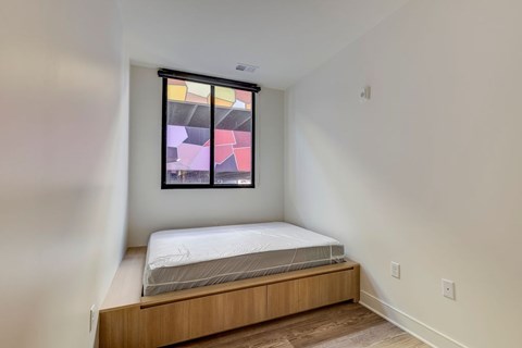 A bedroom with a bed and a window with a colorful abstract painting.