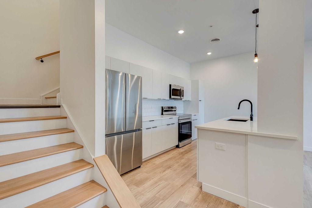 A kitchen with a stainless steel refrigerator and wooden flooring.