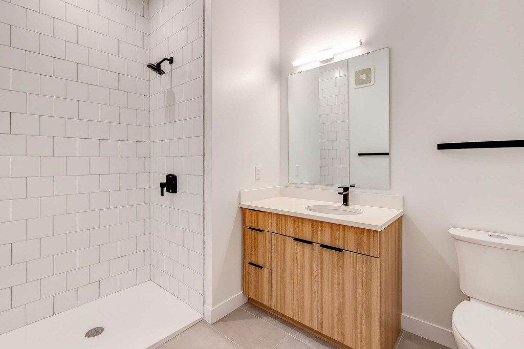 A white bathroom with a wooden vanity and a white toilet.