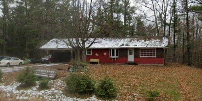 A red house with a white roof is surrounded by trees.