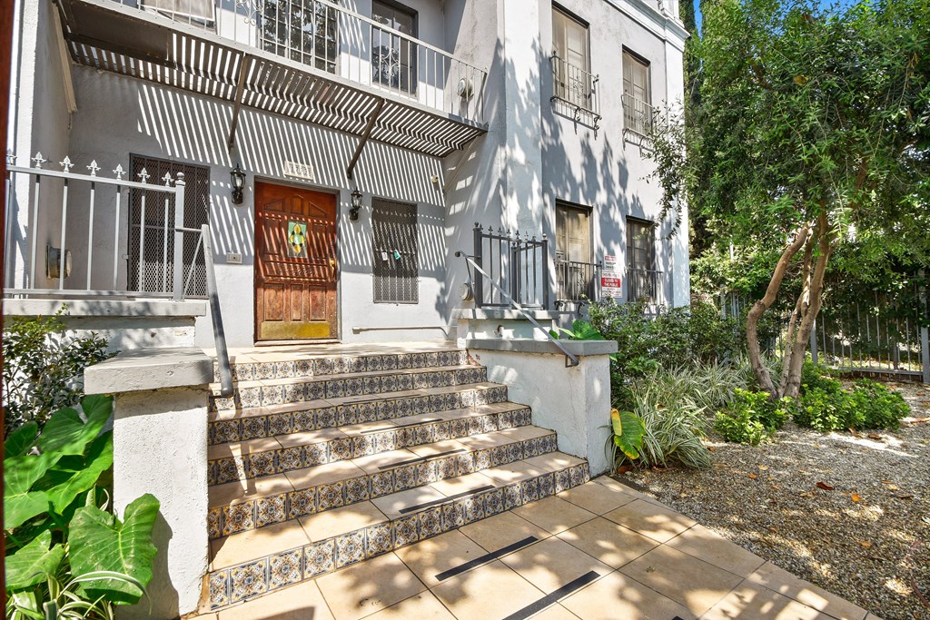 A white building with a brown door and a metal railing.