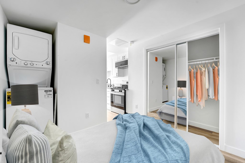 A bedroom with a bed, a couch, a lamp, and a closet with clothes hanging.