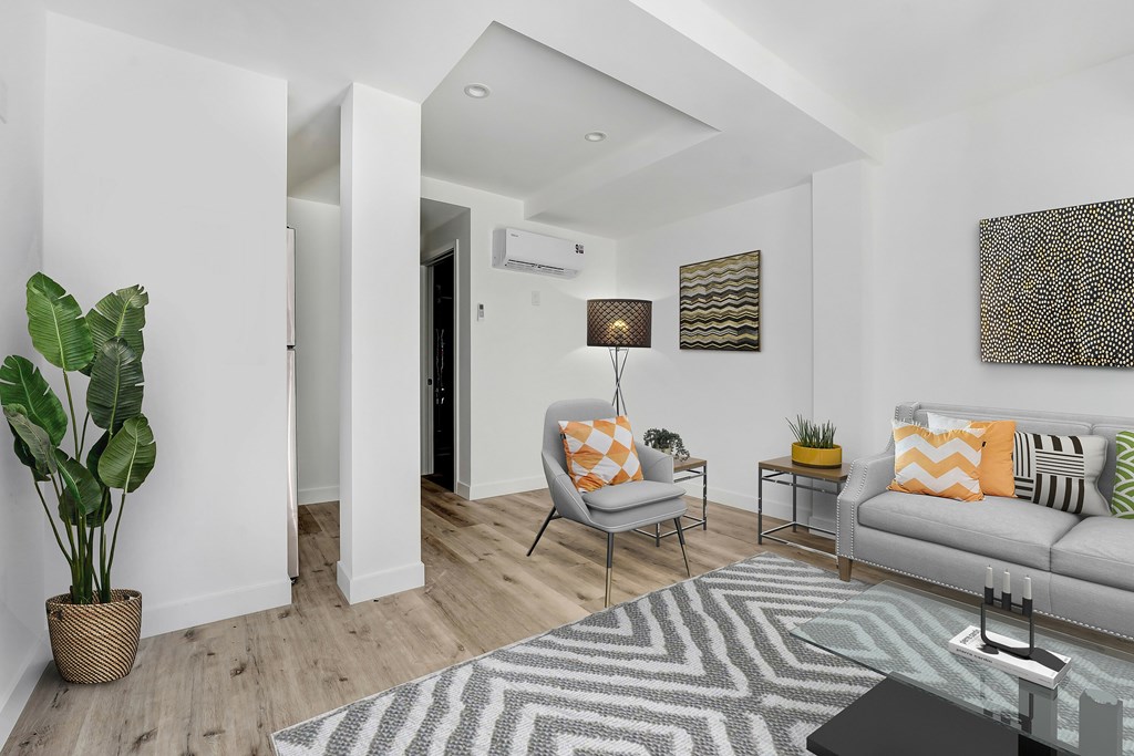 A living room with a white couch, a grey rug, a white chair, a potted plant, and a painting on the wall.