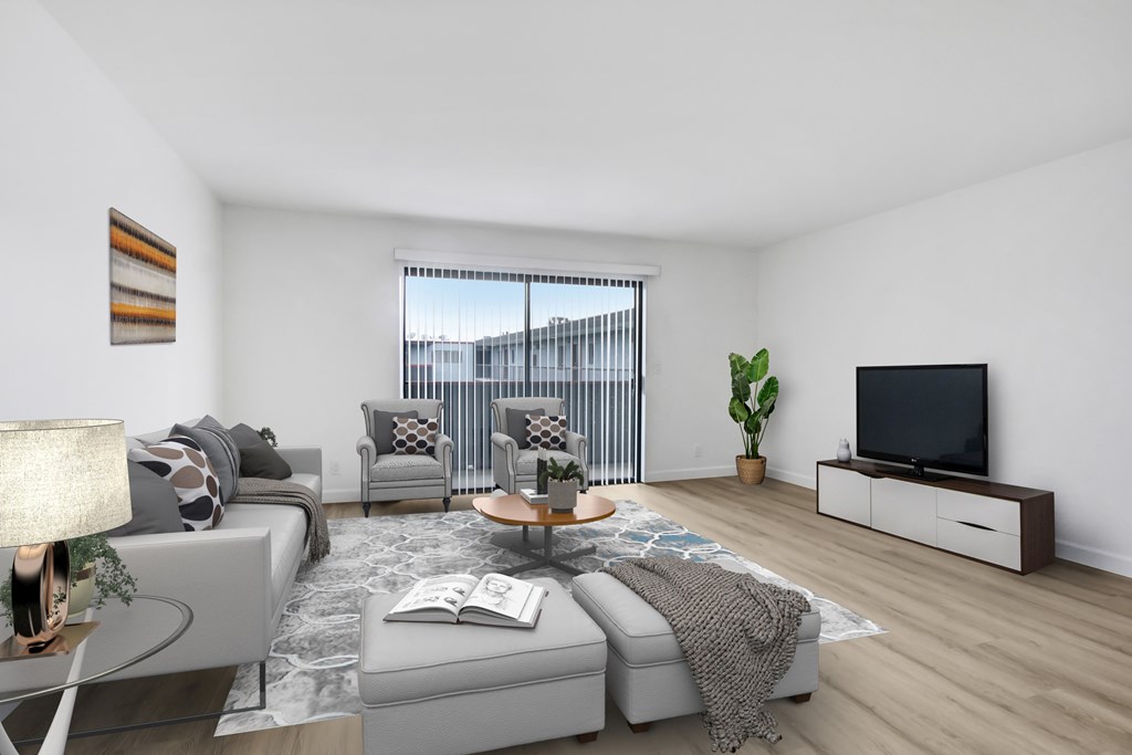A modern living room with a grey sofa, a coffee table, a TV, and a window with a view of a fence.