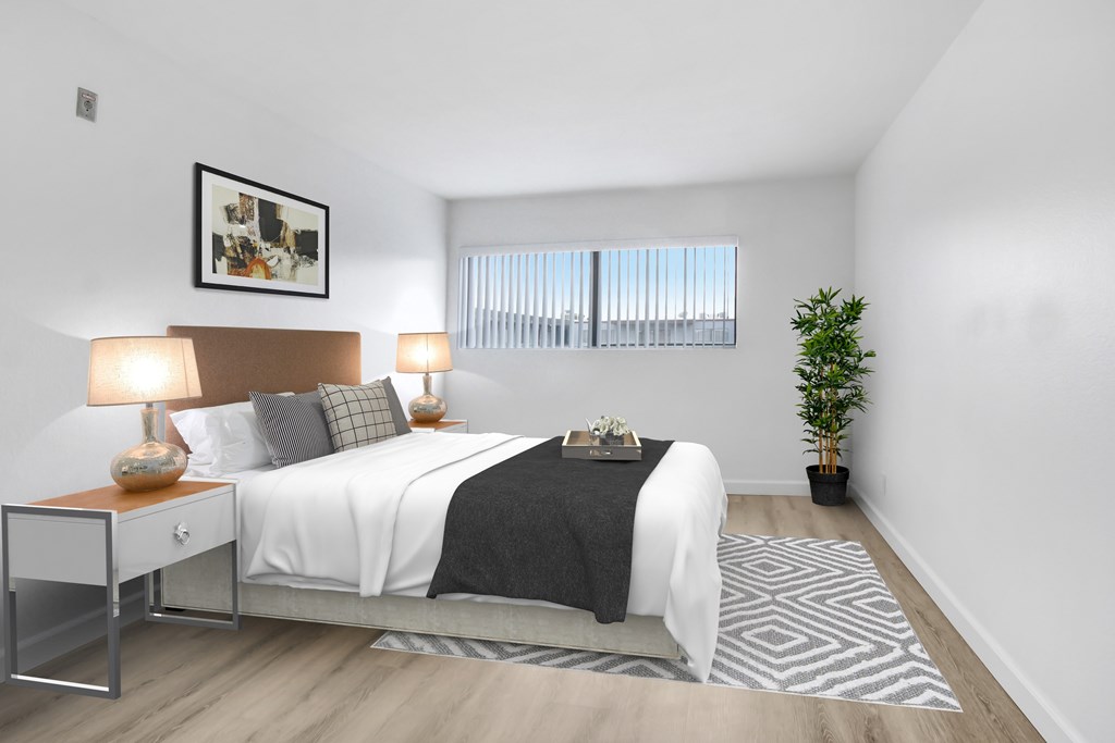 A bedroom with a bed, nightstand, and a plant.