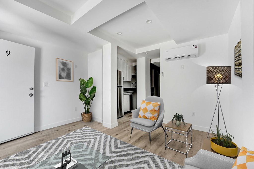 A living room with a grey and white patterned rug, a yellow and white striped pillow on a chair, and a yellow floor lamp.
