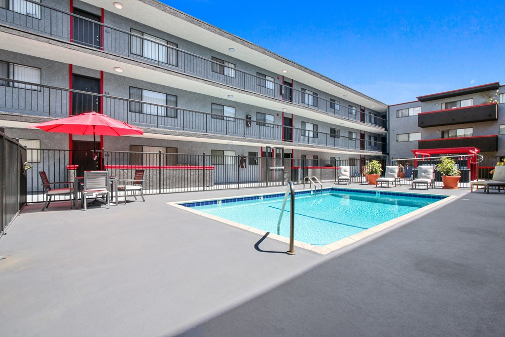 A swimming pool is surrounded by a patio with chairs and umbrellas.