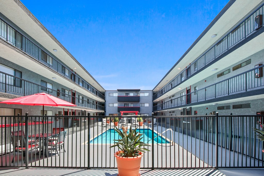 A pool area with red umbrellas and a black fence.