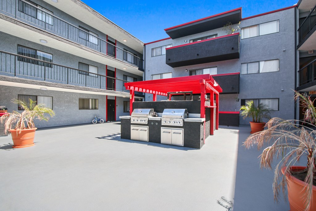 A red awning is over a grill and sink outside a building.