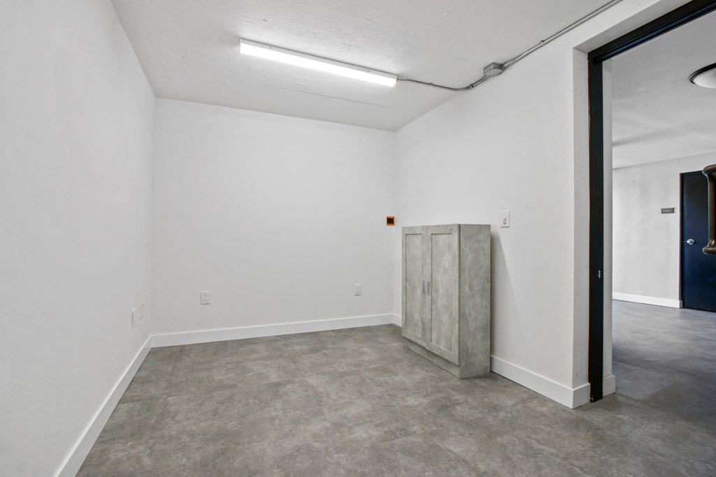 A room with a grey floor and a white wall with a door on the right.