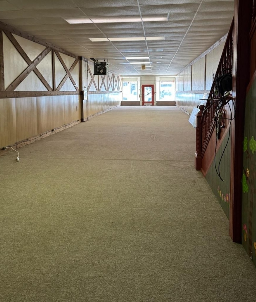A long, empty hallway with a green carpet and wooden walls.