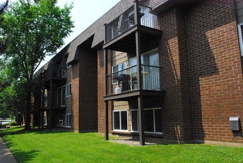 A brick building with balconies and a green lawn in front.