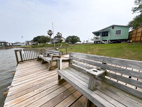 A wooden dock extends into a body of water with a bench and a table on it.