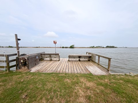 A wooden dock extends into a body of water with a red flag in the distance.