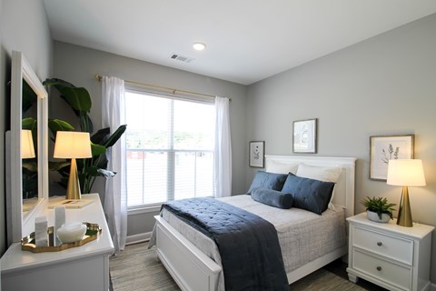A bedroom with a large bed, a nightstand with a lamp, and a dresser with a mirror.
