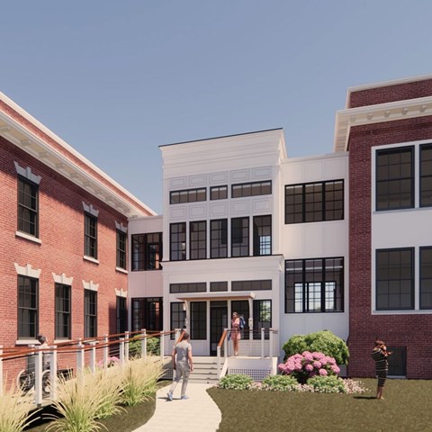 A woman is walking towards a white building with a red brick building behind her.