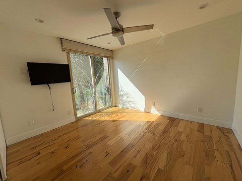 A room with a ceiling fan and a flat screen TV mounted on the wall.
