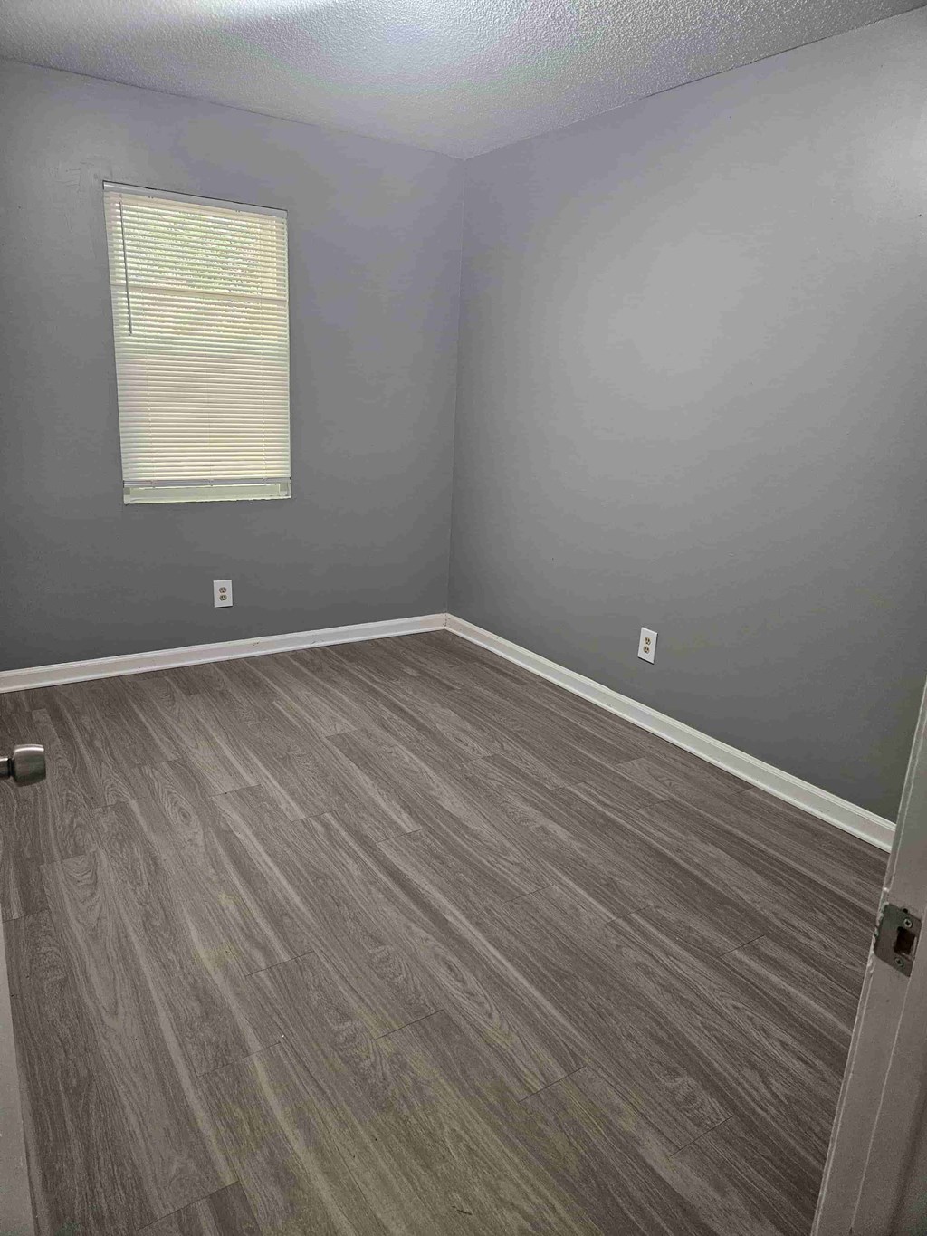 A room with a grey floor and a window with blinds.