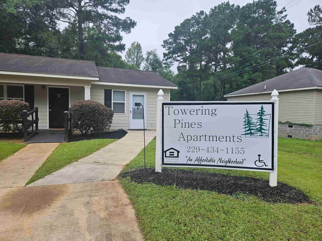 A sign for Towering Pines Apartments is in front of a building.