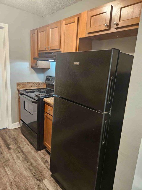 A black refrigerator in a kitchen with wooden cabinets.