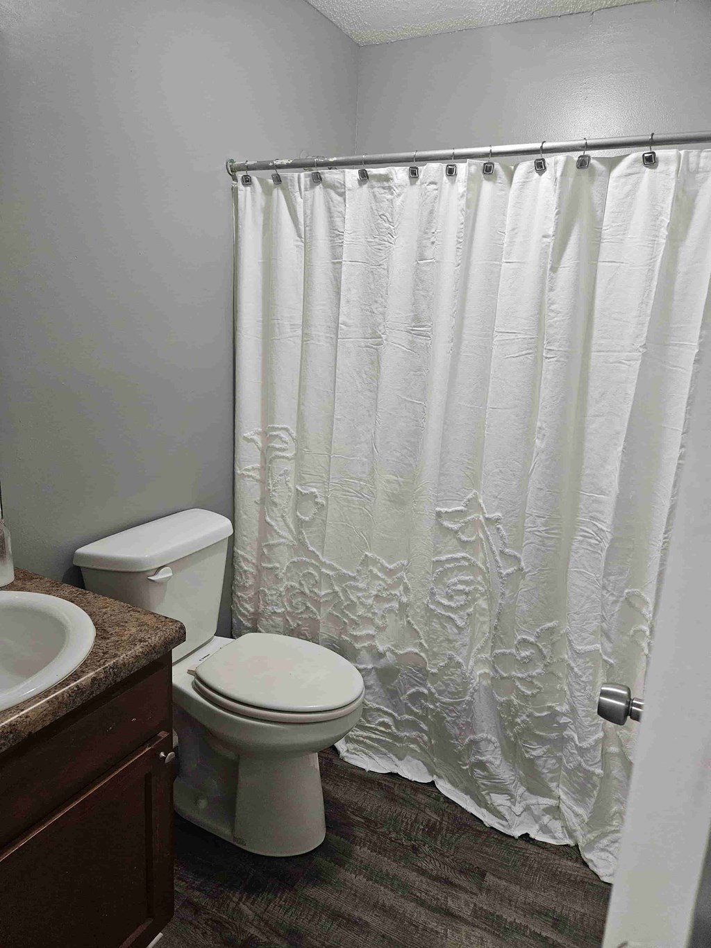 A white shower curtain with lace design hangs in a bathroom.