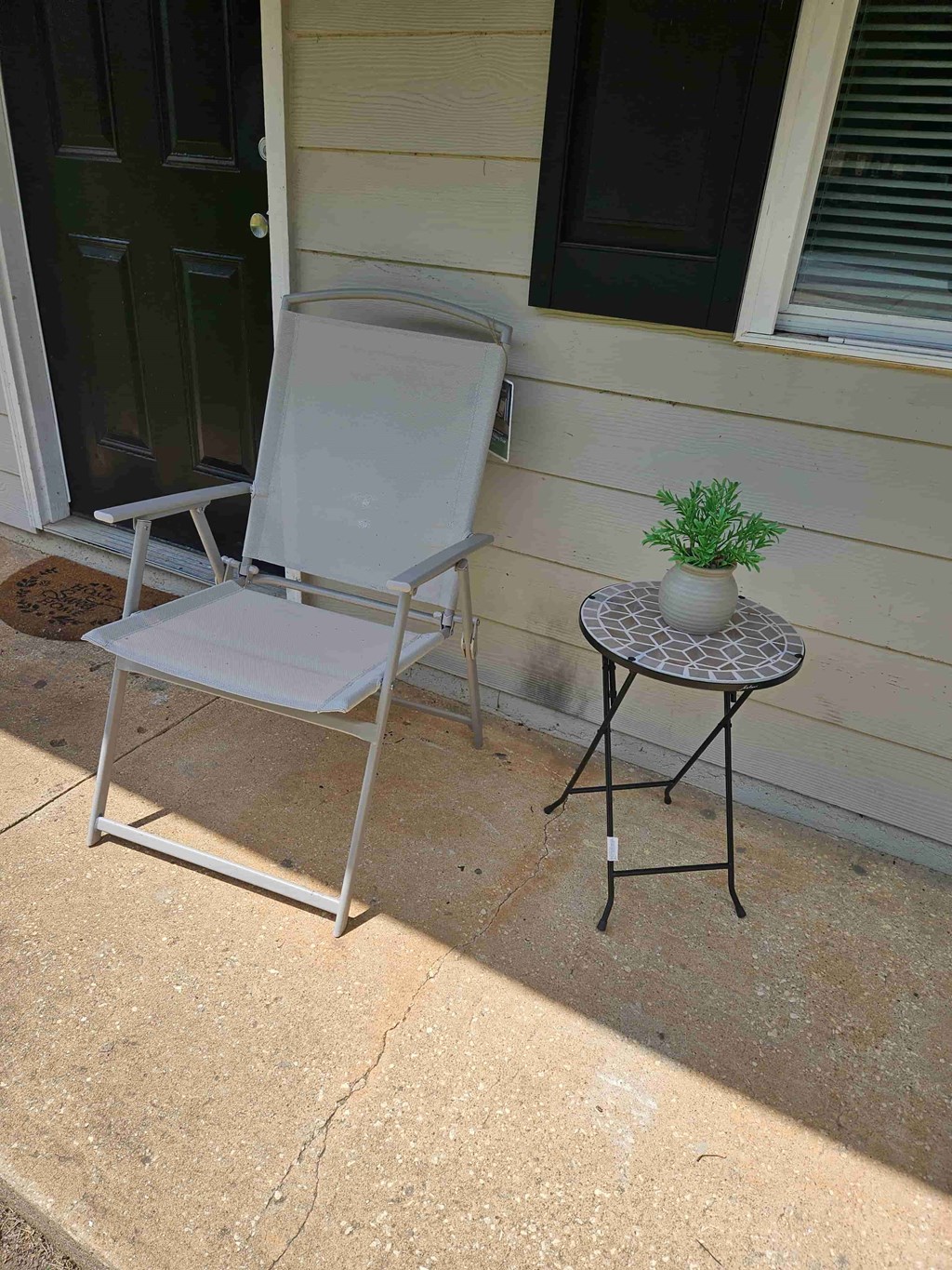 A white chair and table with a plant on it are on a patio.