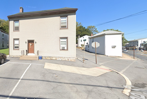A two-story house with a garage is situated in a parking lot.