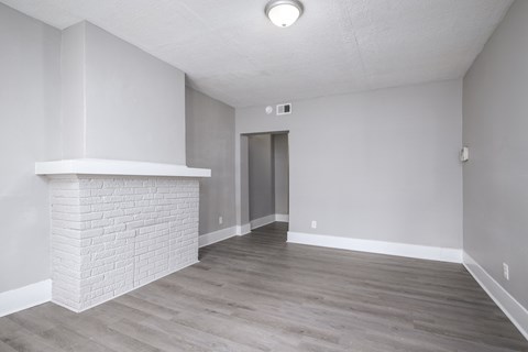 A room with a white brick fireplace and wood flooring.