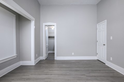 A room with a white door and a hallway leading to another room.