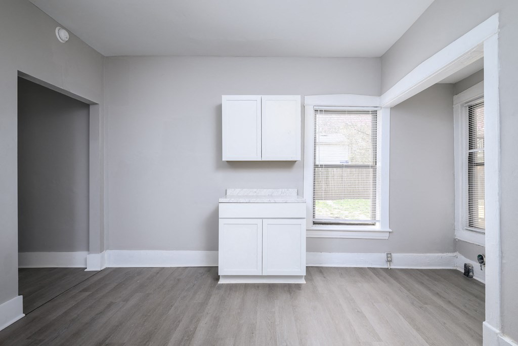 A white cabinet sits in a room with light grey walls and a wooden floor.