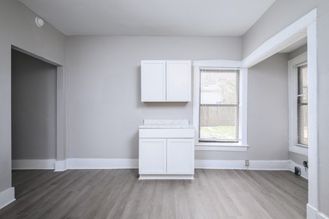 A white cabinet sits in a room with light grey walls and a wooden floor.