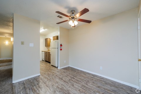 A room with a ceiling fan and a refrigerator in the background.