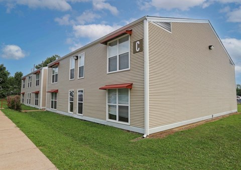 A beige house with a red roof and a green lawn in front.