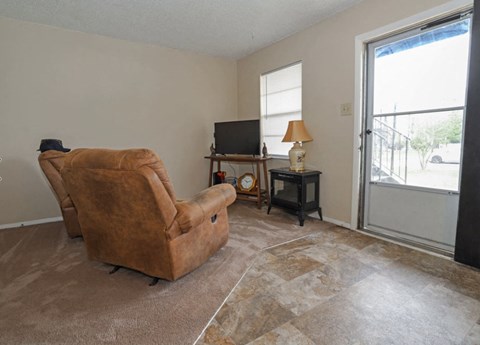 A living room with a brown chair, a small table with a lamp, and a television.
