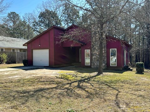 A red barn-like building with a white garage door is surrounded by trees.