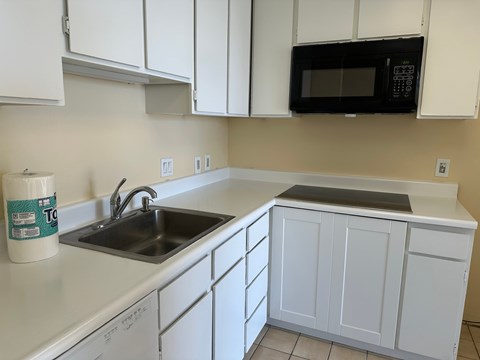 A kitchen with white cabinets and a black microwave above the sink.