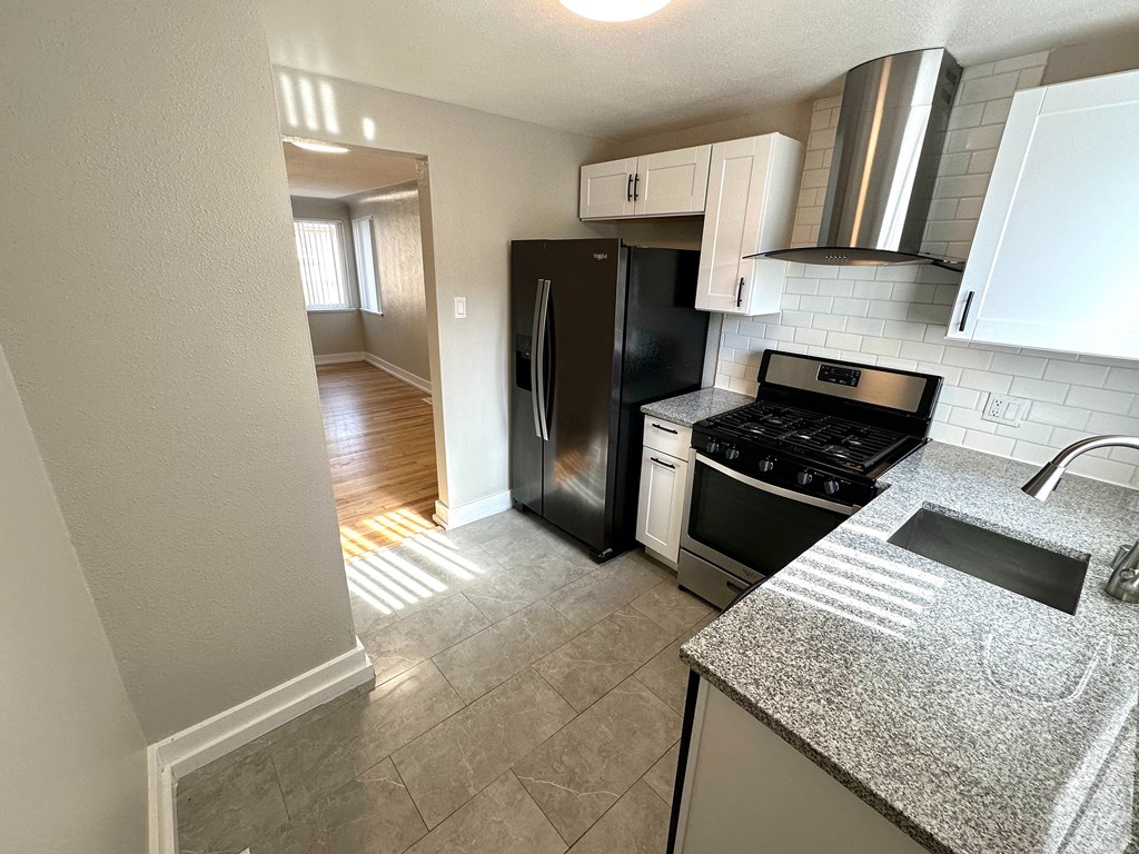 A kitchen with a black refrigerator, white cabinets, and a granite countertop.