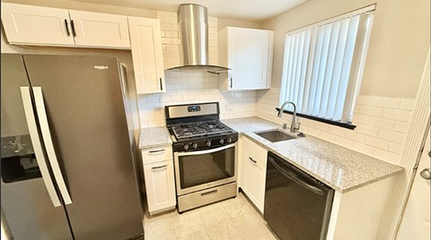 A kitchen with a black refrigerator, white cabinets, and a granite countertop.