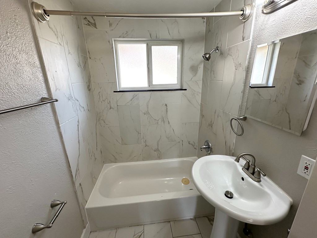 A white sink is in a marble bathroom with a window.