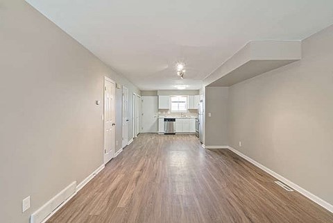 A long, empty hallway with wood flooring and white walls.