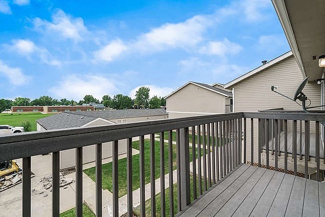 A balcony with a black railing overlooks a grassy area and other houses.