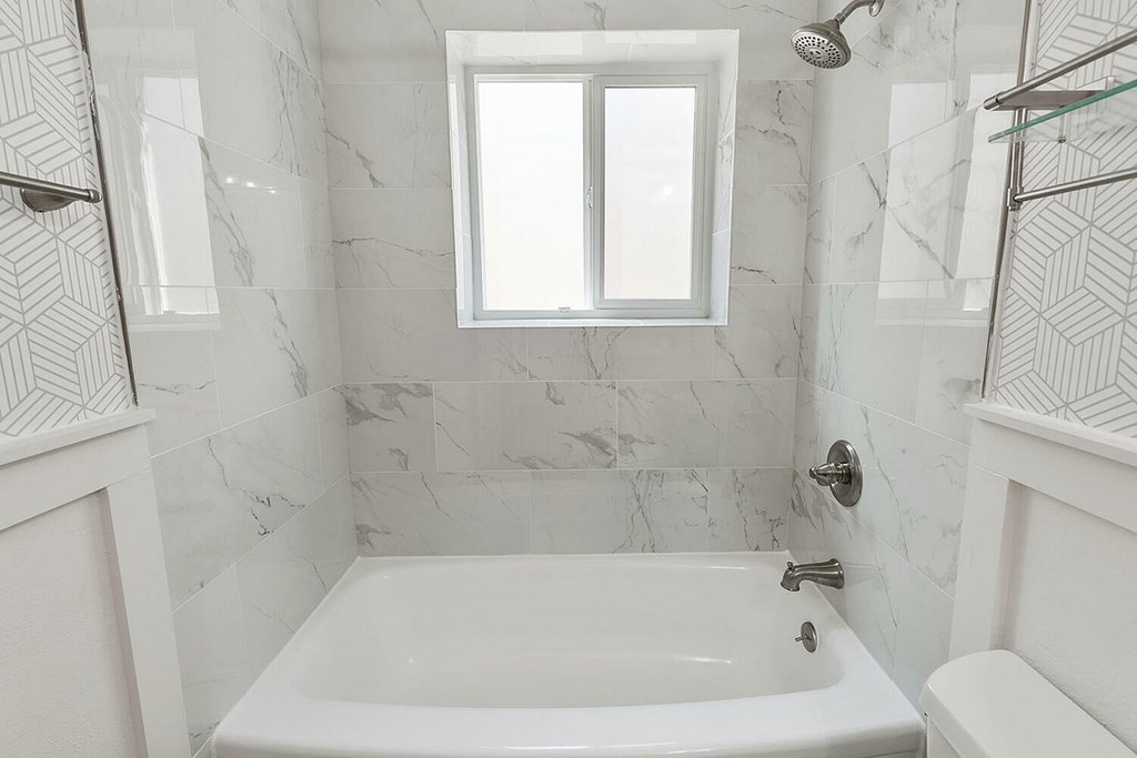 A white bathroom with a marble tile wall and a window.