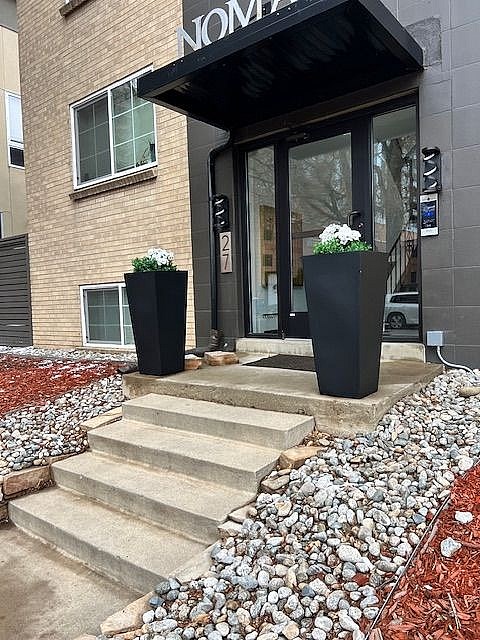 A modern two-story building with a black awning and a red brick pathway leading to the entrance.