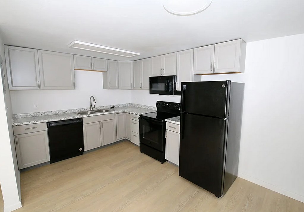 A black refrigerator stands in a kitchen with white cabinets and a marble countertop.