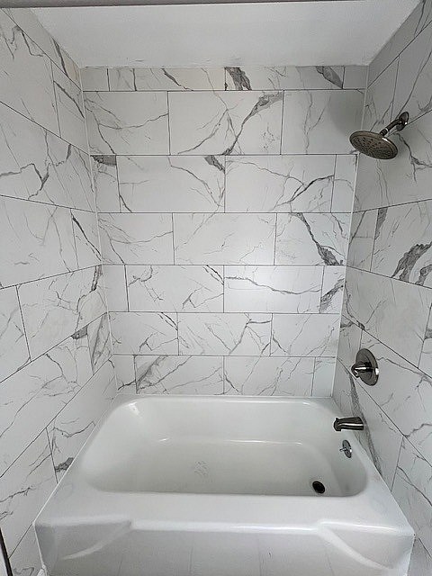 A white bathtub with a marble tile wall.